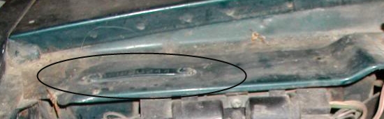 Located to the side of the hinge bolts on the front.